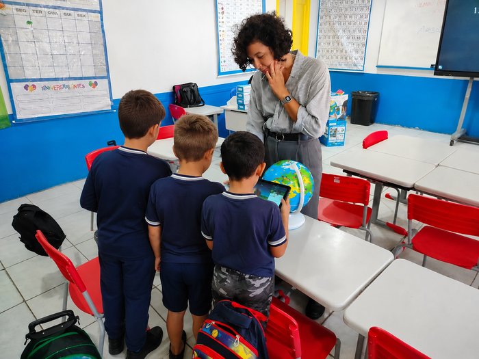 Turma reunida em sala de aula explorando um globo interativo com a professora